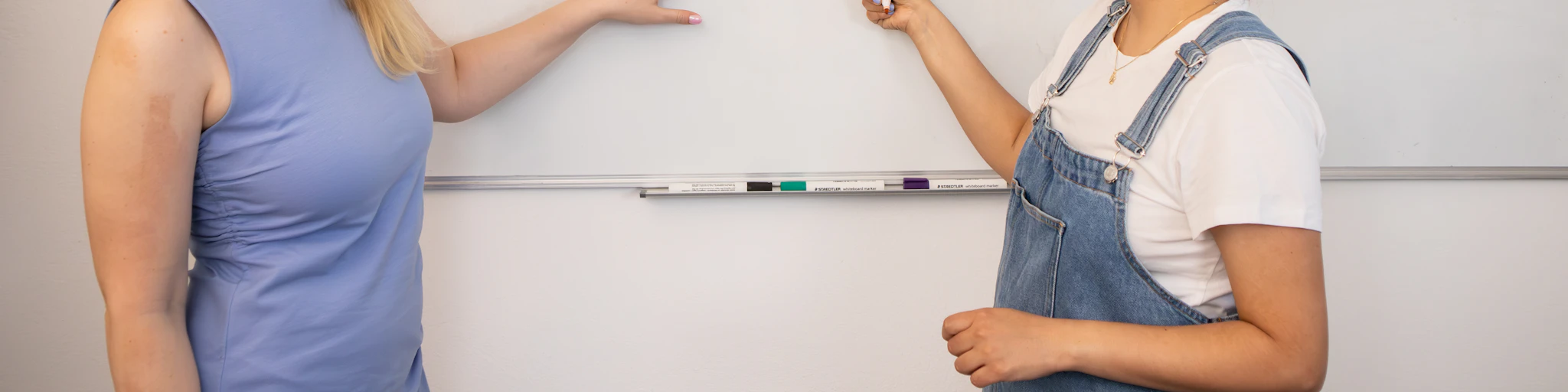two women standing in front of a whiteboard with writing on it