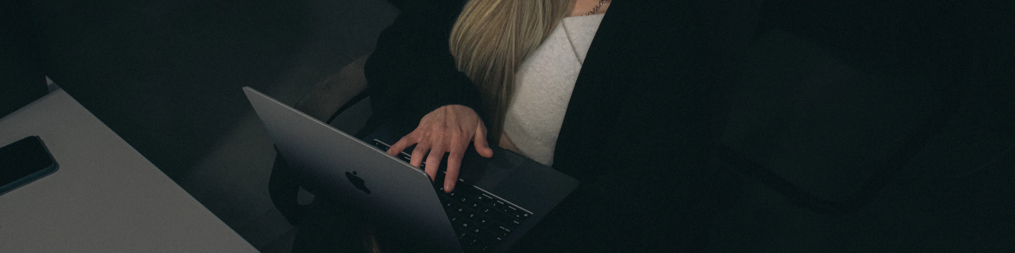Woman working late on a laptop in a dark office.